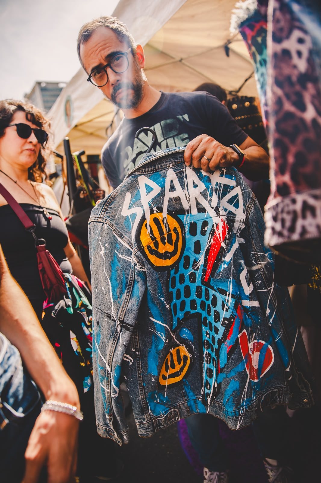 Expositor segurando uma jaqueta jeans pintada à mão com a palavra Sparta, carinhas sorridentes e raio